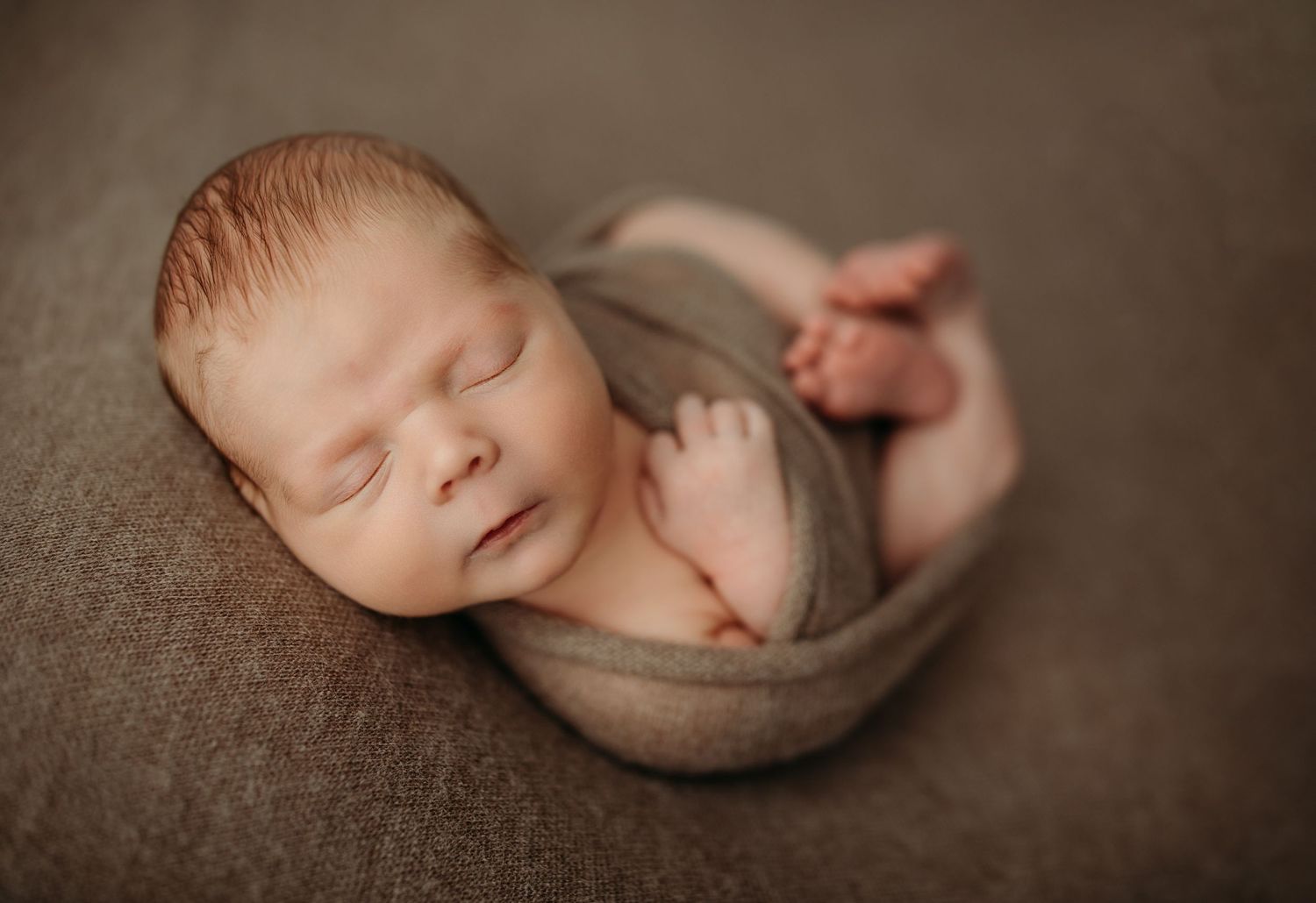 Professional newborn photography with baby wrapped in soft neutral fabrics.
