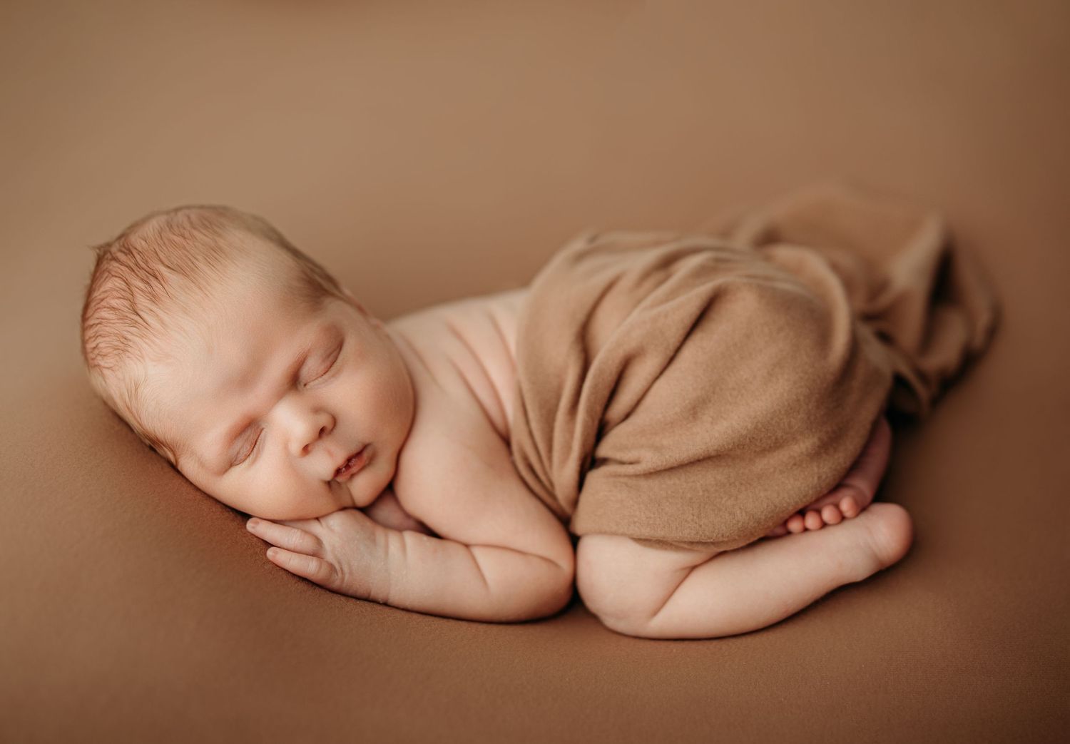 Peaceful sleeping newborn baby posed in artistic nude portraits with brown backdrop.
