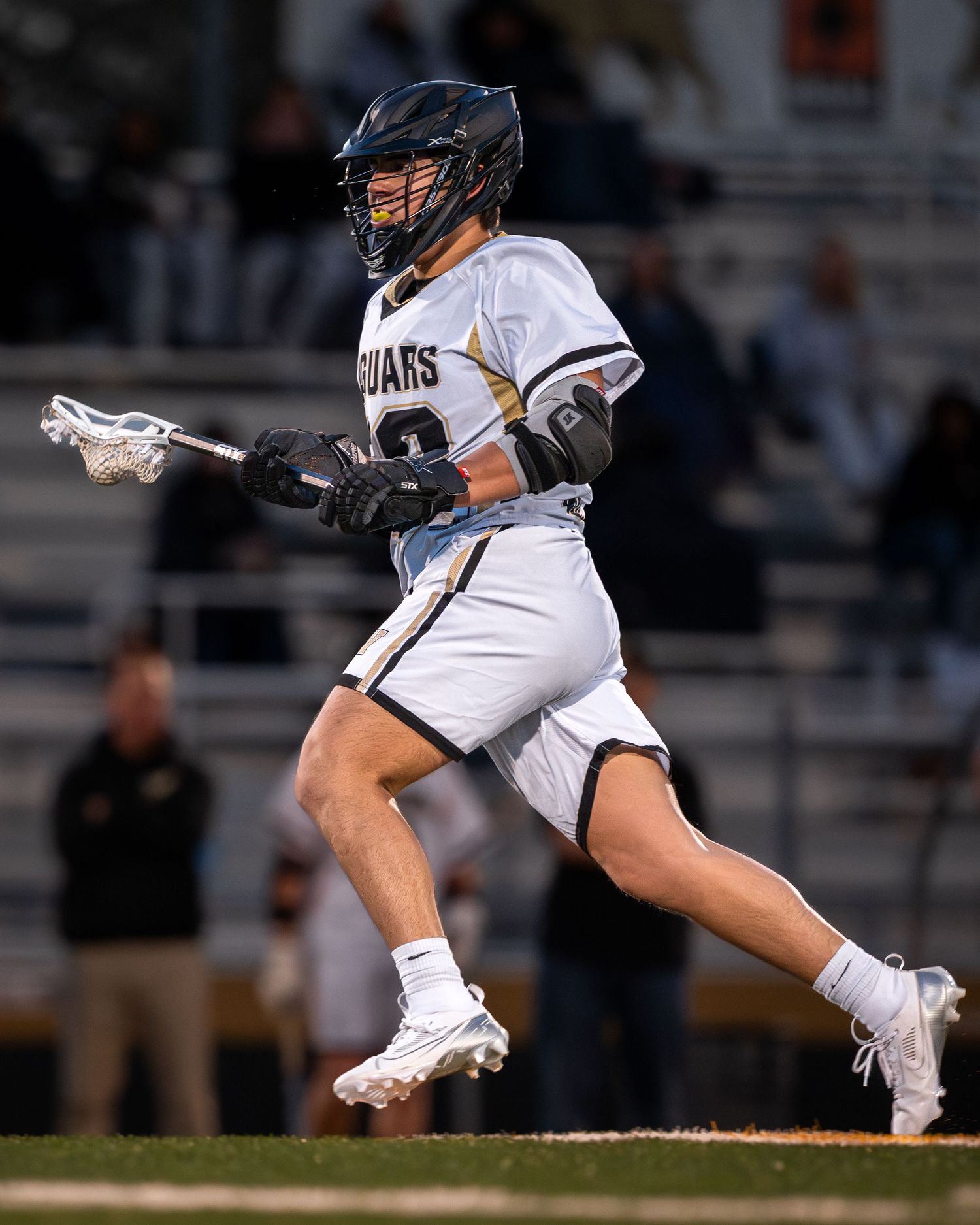 Lacrosse player in white uniform running with a stick during a night game on the field.