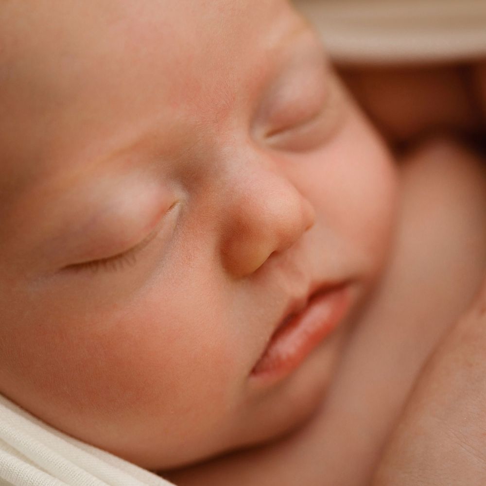 Close up of a sleeping baby's peaceful face resting on soft white fabric.