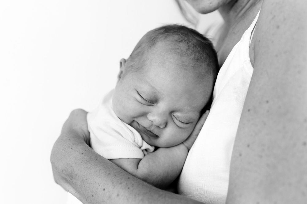 A sleeping newborn baby in black and white rests peacefully in someone's arms.