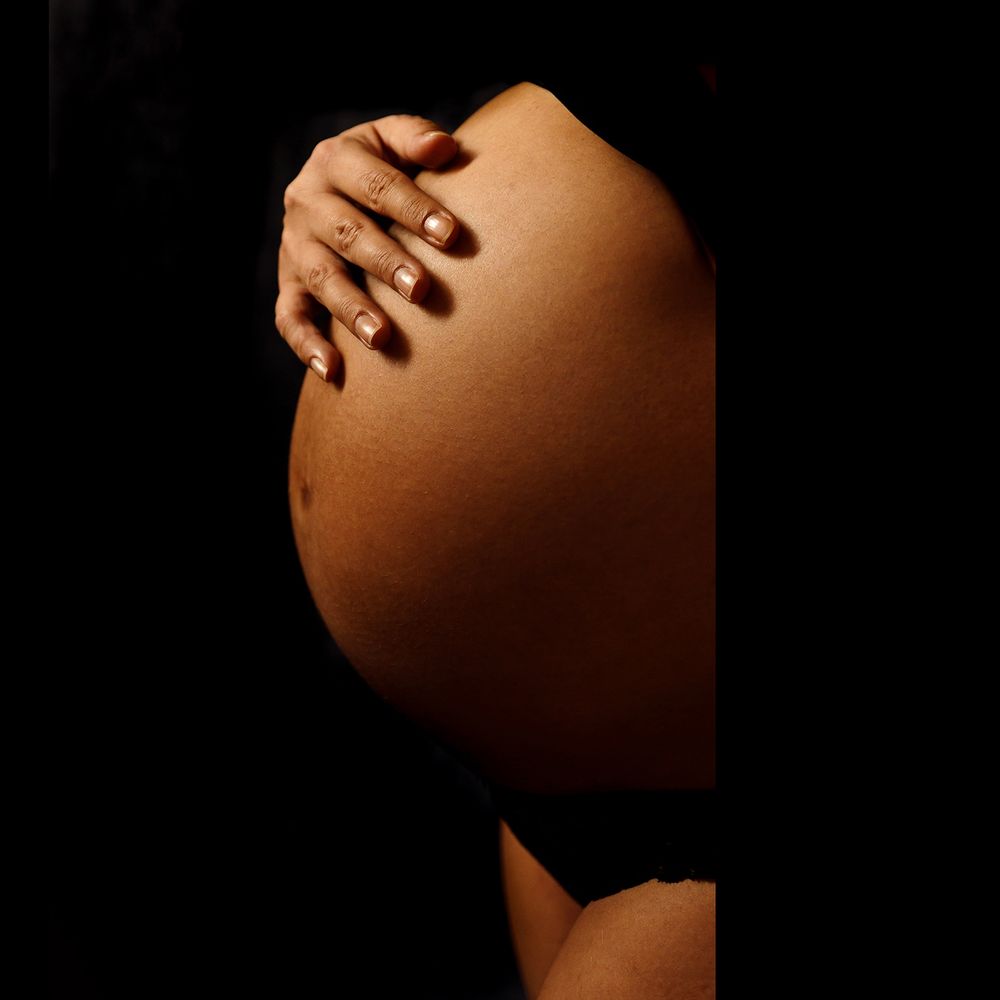 Dramatic artistic pregnancy photo showing silhouette of pregnant belly against dark background with hand resting on bump.