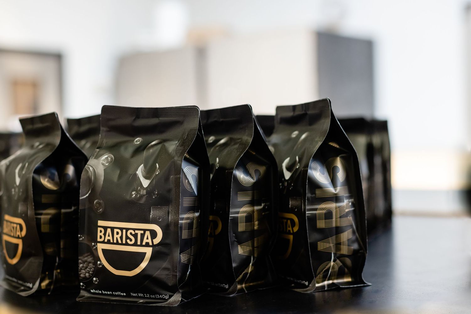Black barista coffee bags lined up on a counter showing premium packaging and branding details in shallow focus.