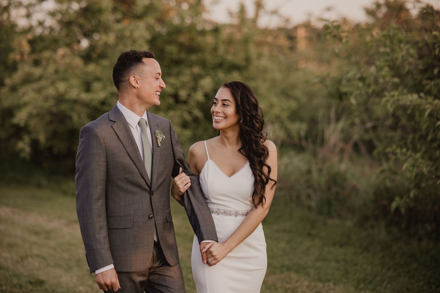 A couple in wedding attire share a joyful moment together in a lush garden setting at sunset.