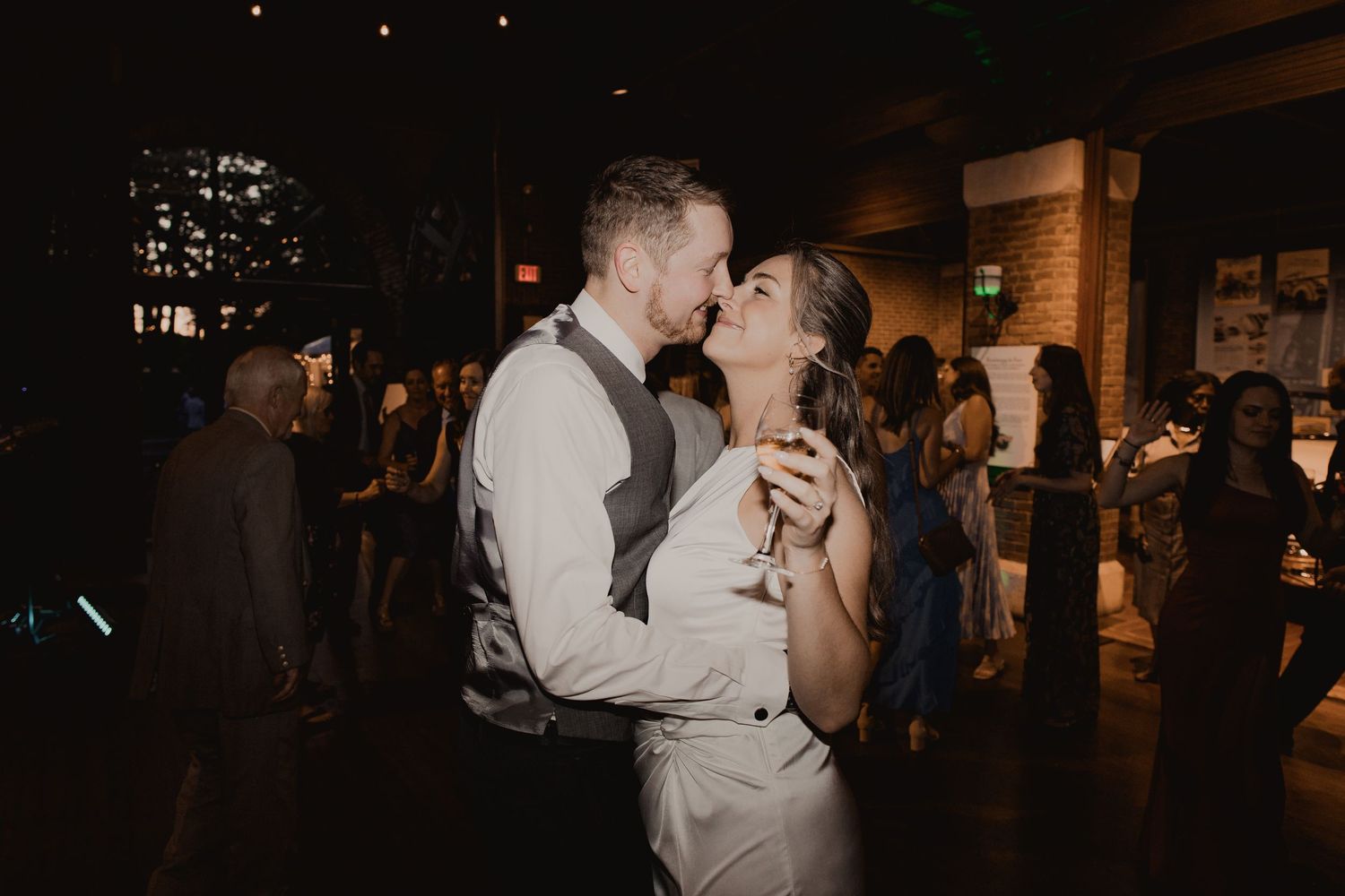 A romantic moment between a couple dancing and sharing champagne in a dimly lit reception venue.