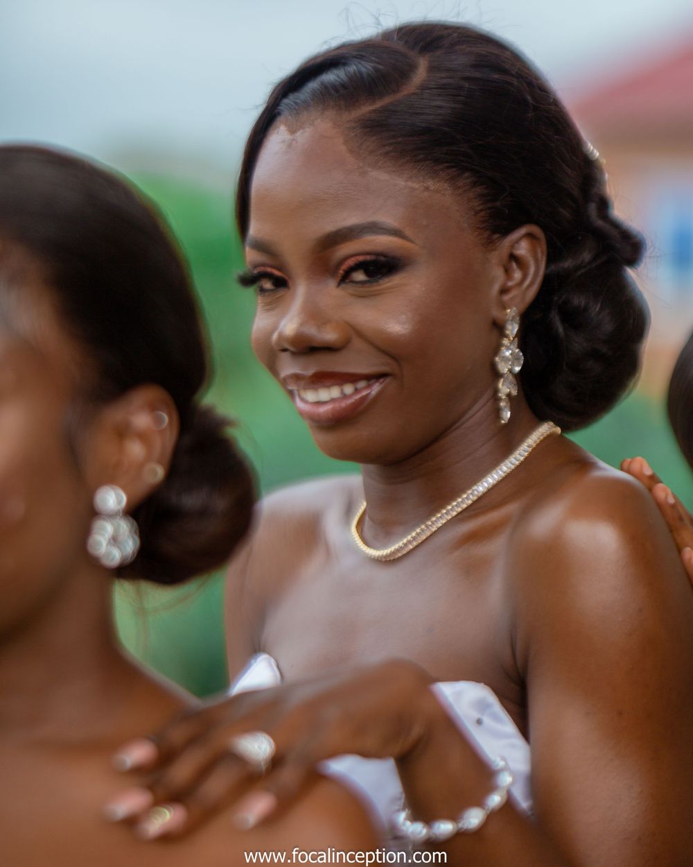 Elegant bride smiles warmly while wearing a white wedding dress, pearl necklace and dangling crystal earrings.