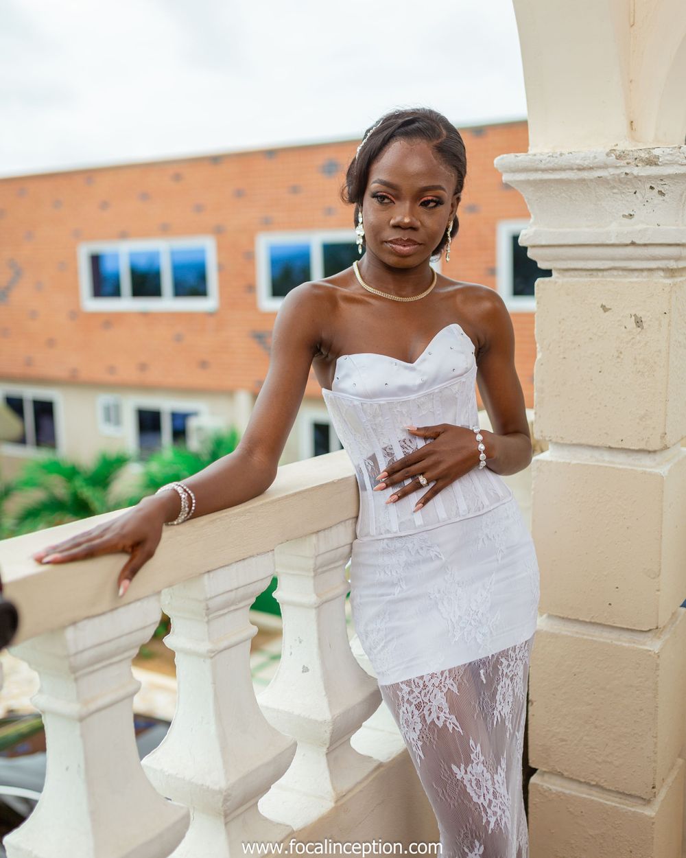 Wedding portrait in a white lace dress posing elegantly on a balcony with cream columns.