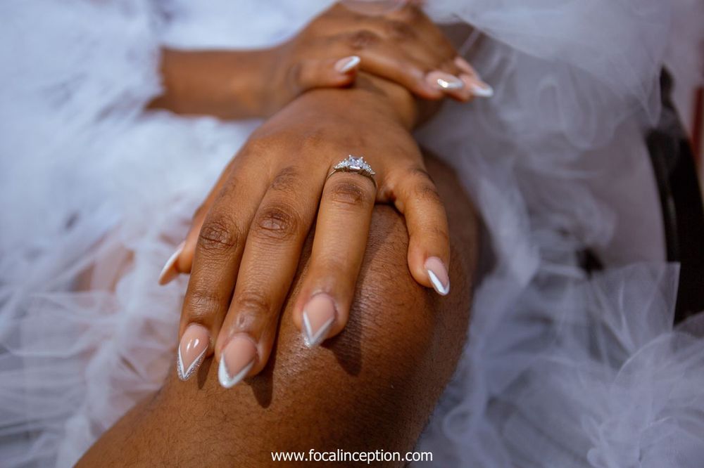Close-up of beautifully manicured hands with white nails and an engagement ring resting on soft white tulle fabric.