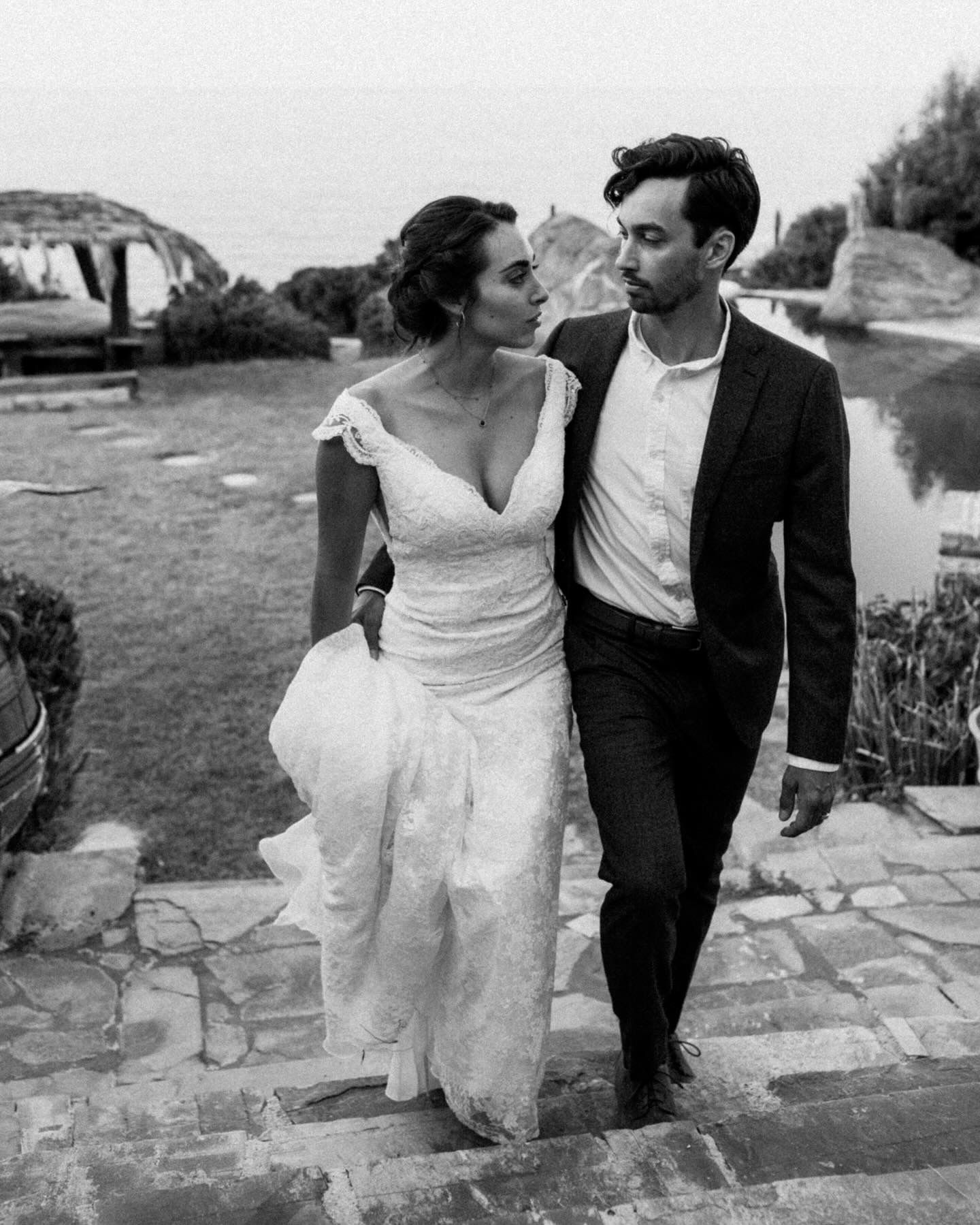 A romantic black and white wedding photo of a couple walking together on stone steps, with the bride wearing a flowing dress.