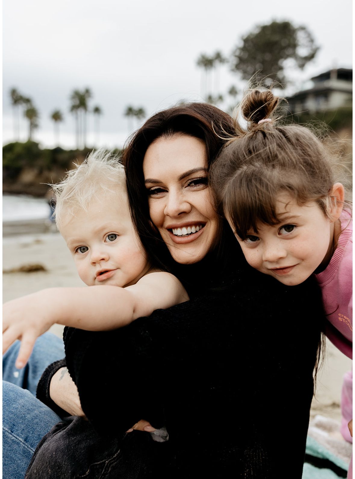 Parent and children smiling together at the beach with palm trees in background.