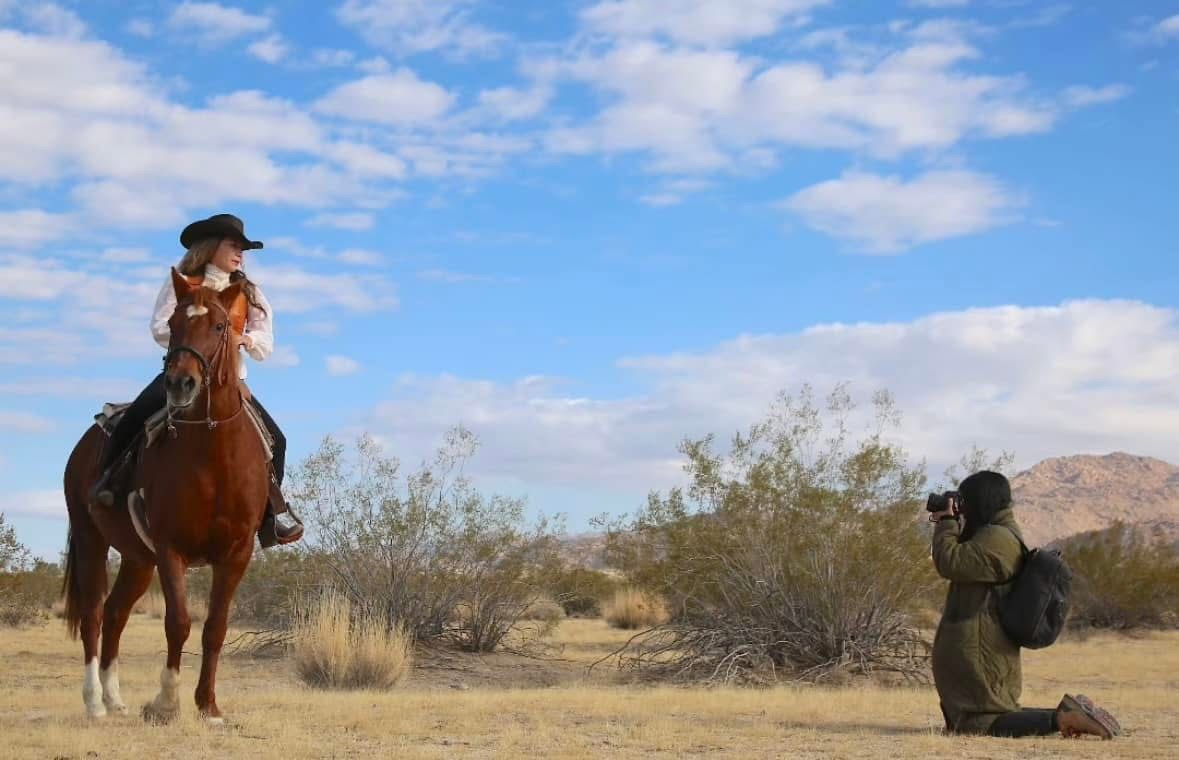 A person on horseback poses for a photograph in a desert landscape.