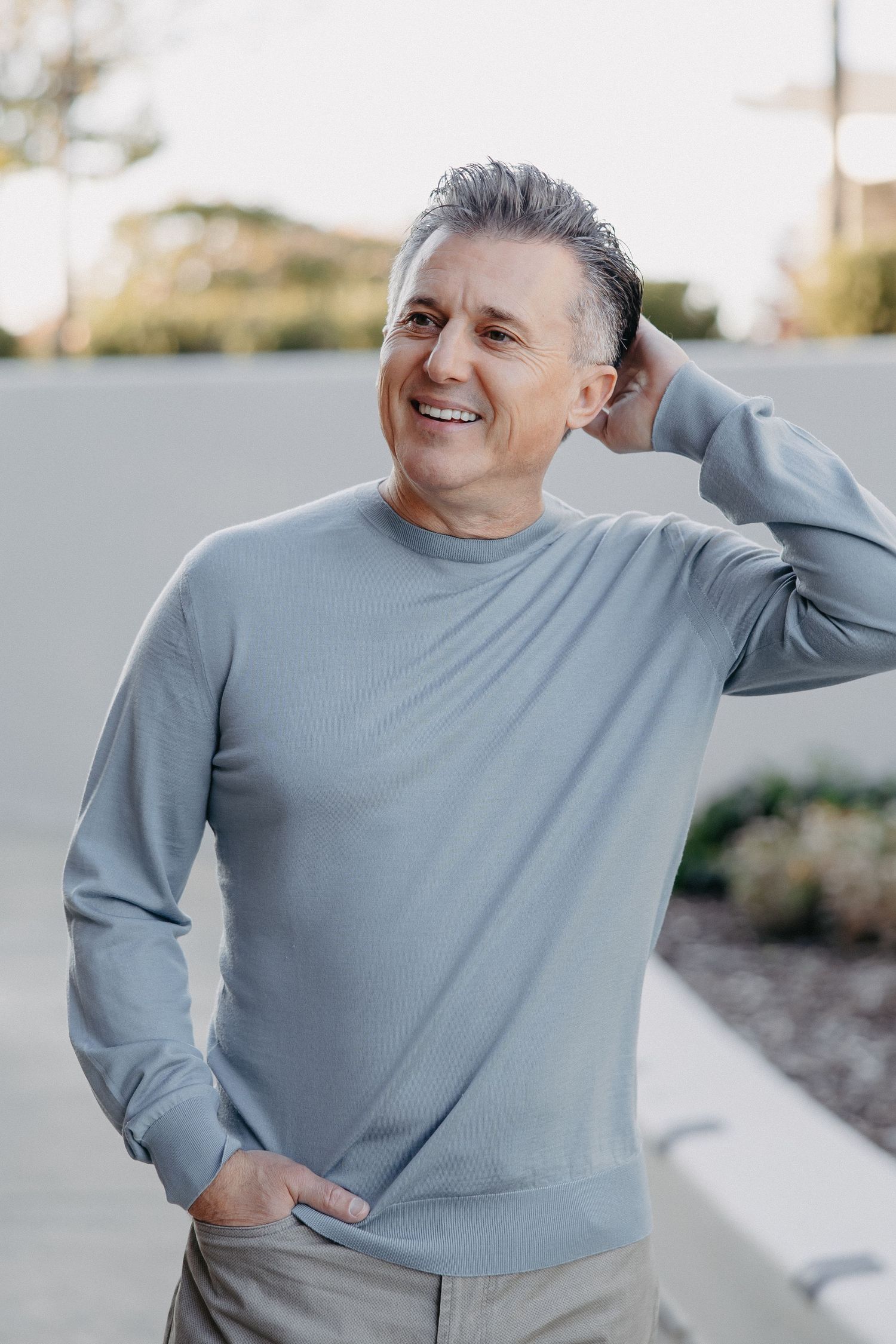 Person wearing a light gray sweater smiles while standing outdoors on a sunny day.