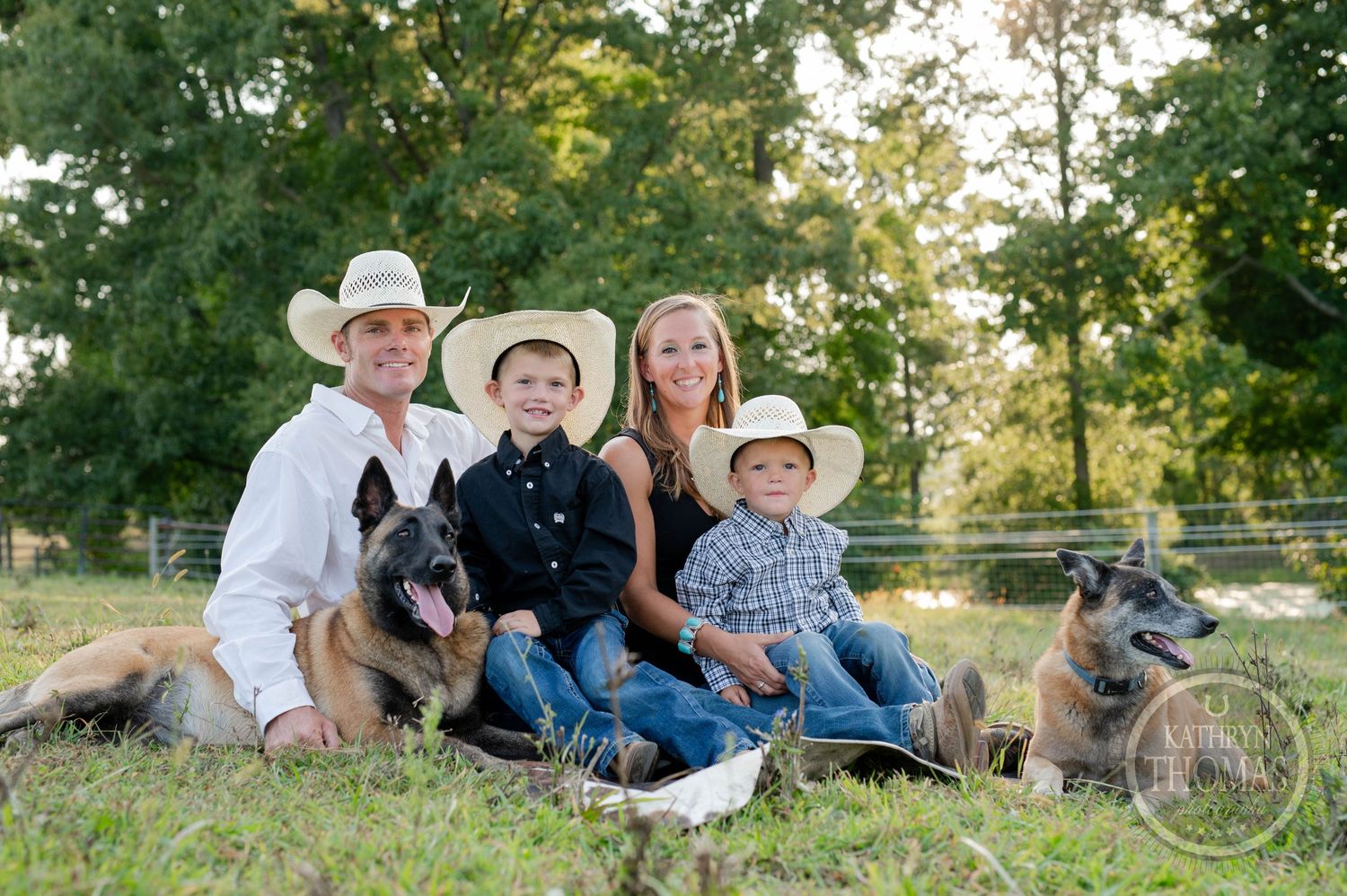 Family portrait with German Shepherd dogs sitting together on grassy hill during sunset.