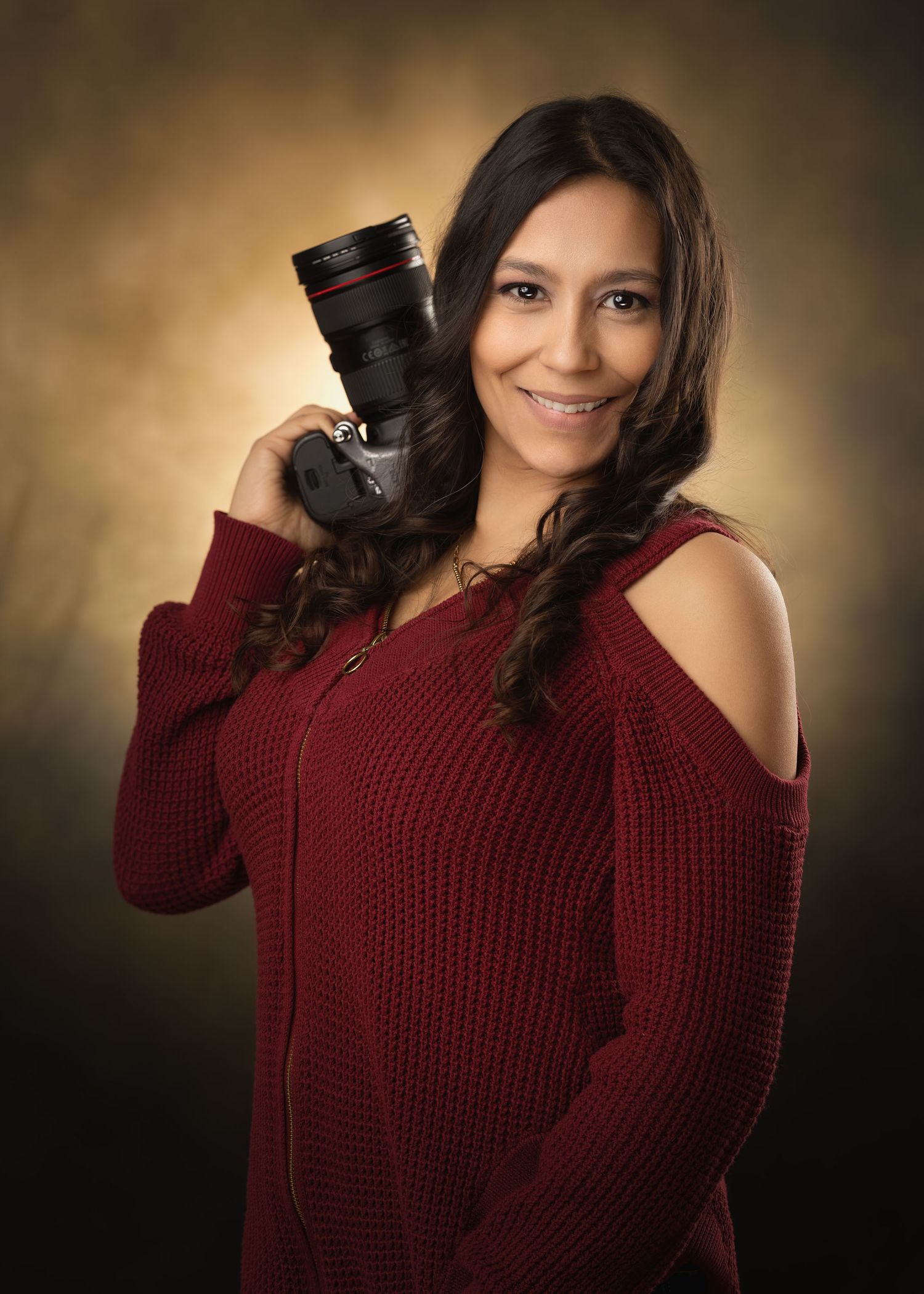Portrait of photographer holding professional camera wearing burgundy sweater.