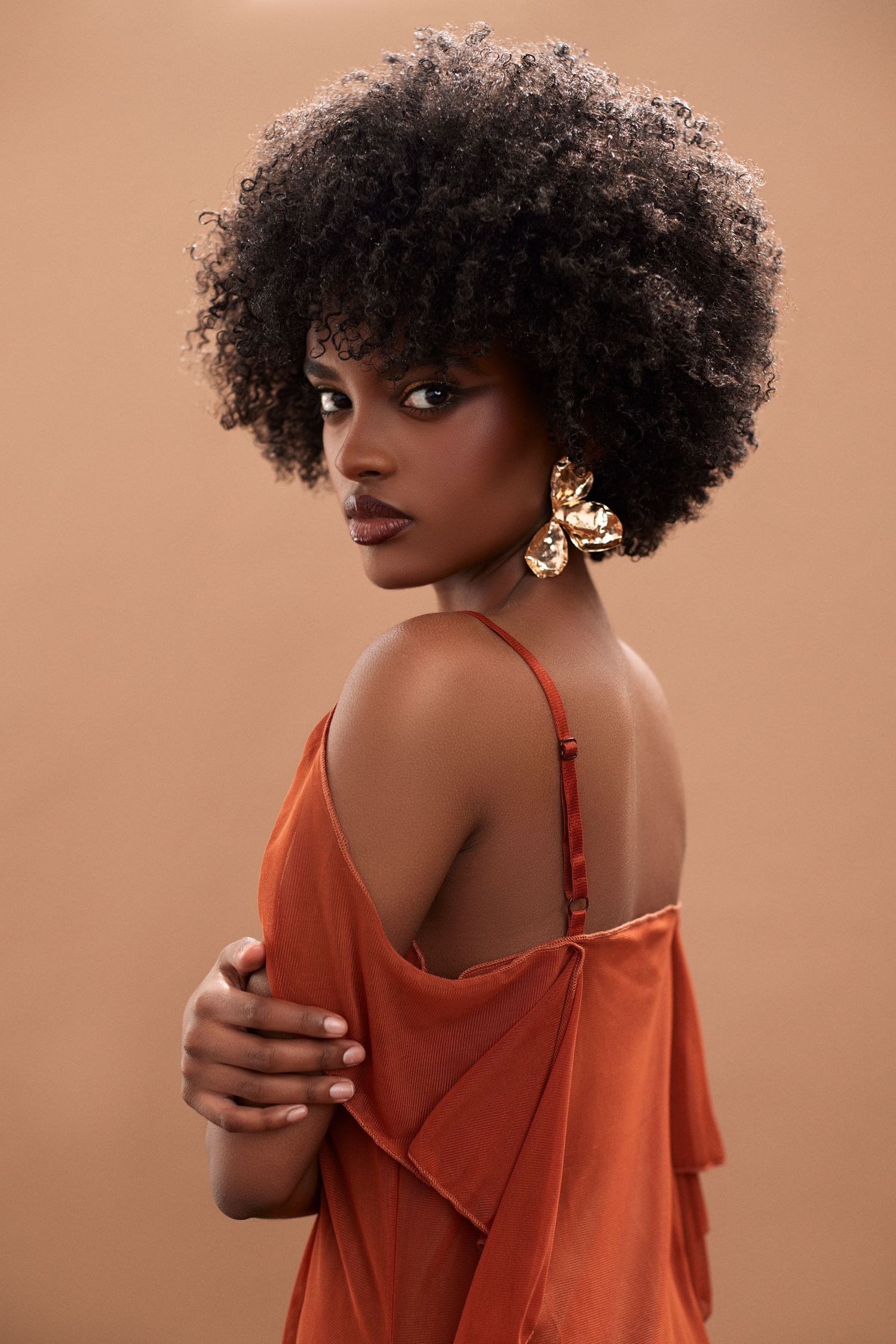 Fashion portrait series showing model in orange top with natural curly hair against peach background.