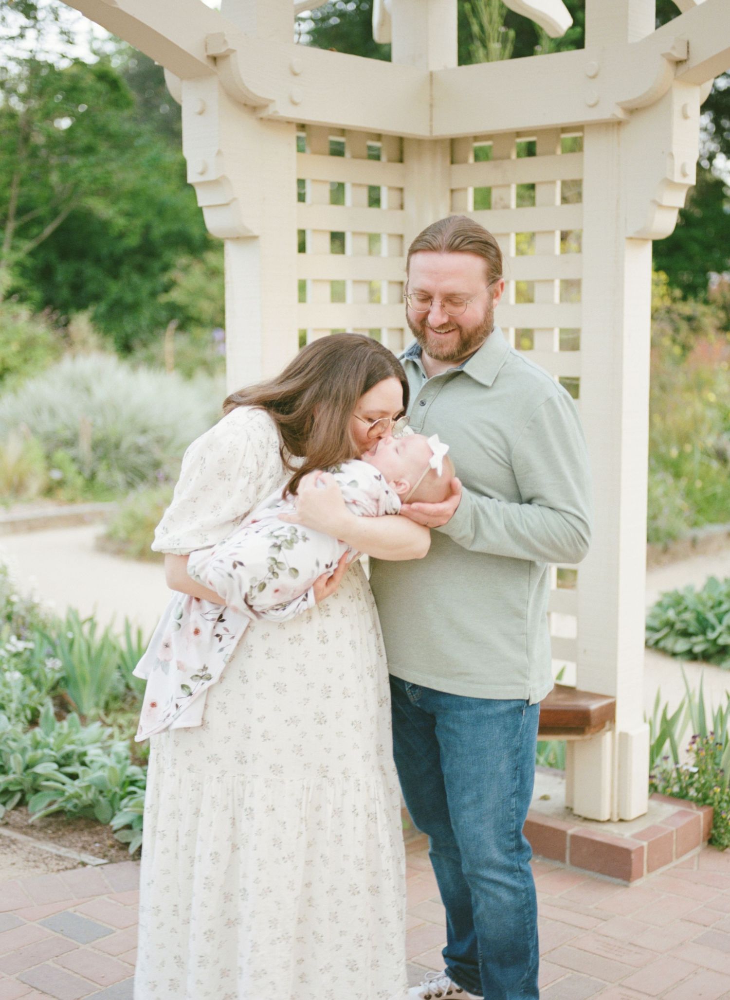 A tender family moment shared under a white garden gazebo with lush greenery in the background.