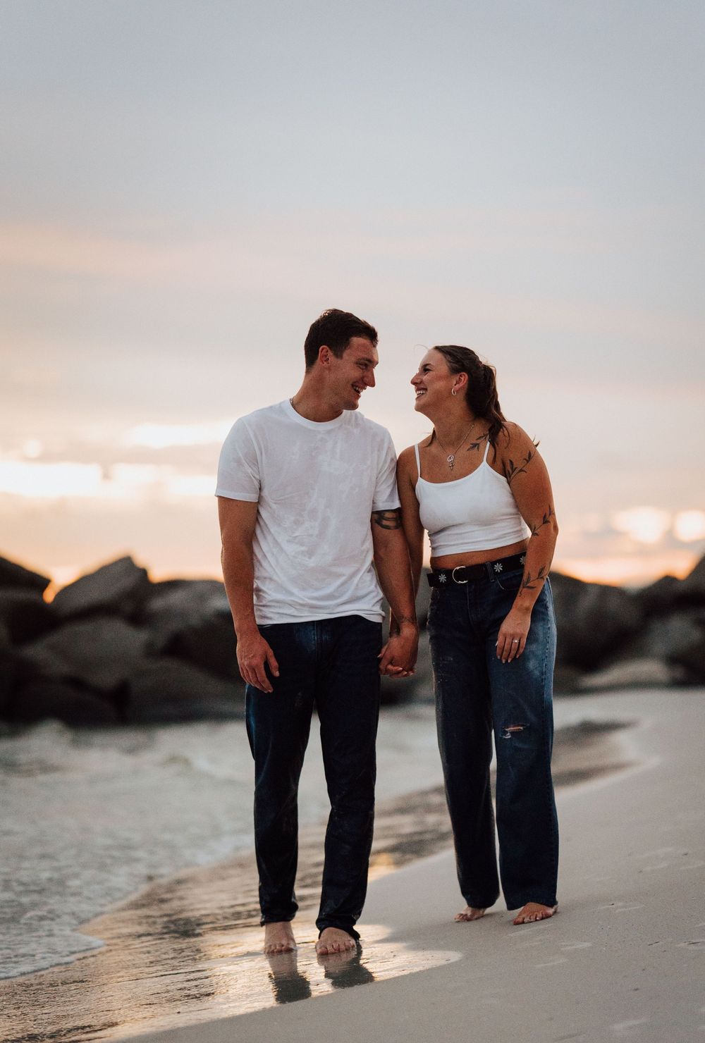 Couple walking hand in hand along a beach at sunset with rocks in the background in St. Pete Tampa Florida