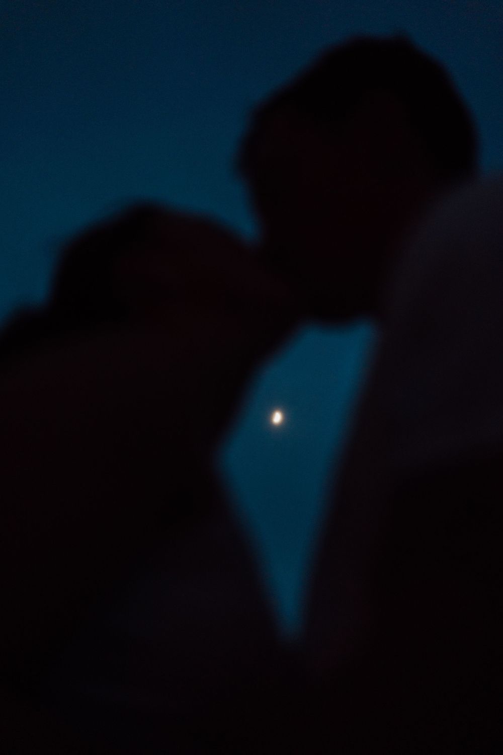 Silhouetted figures in a romantic moment against a dark blue sky with a glowing full moon for engagement photoshoot in Tampa Florida