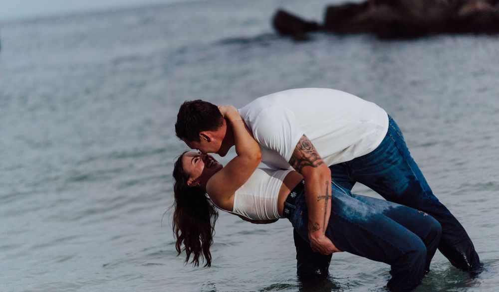 A couple wearing jeans posing for engagement photoshoot by the beach with direct flash photography in St. Pete Florida