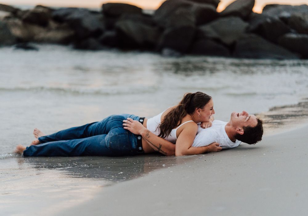 A couple wearing jeans laying down on the sand for engagement photoshoot by the beach with direct flash photography in St. Pete Florida