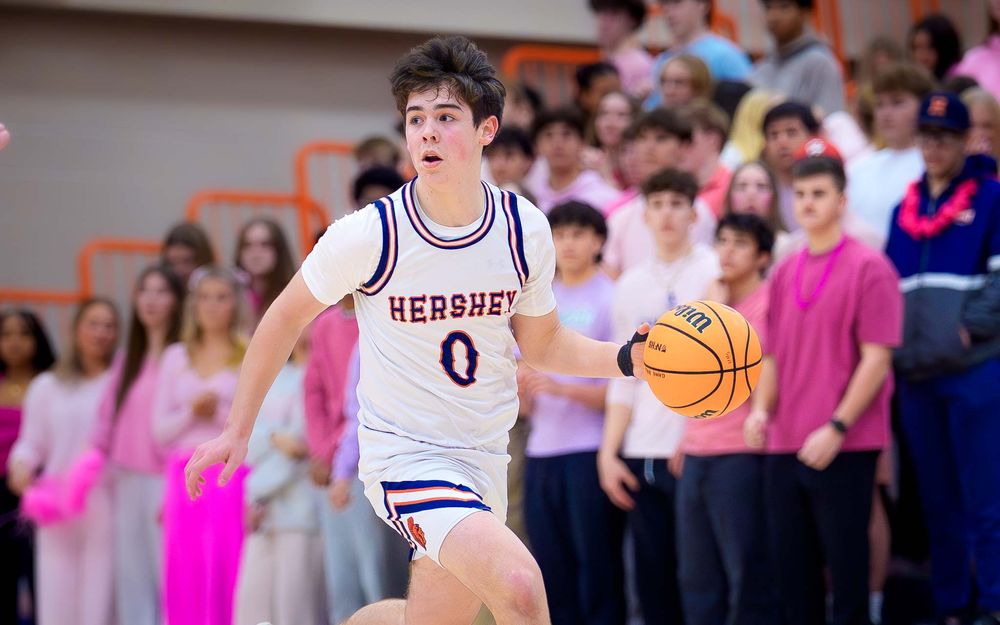 Trojans player dribbles upcourt with focus, pink-clad fans in the background by SportsFox Photography, Hershey PA.