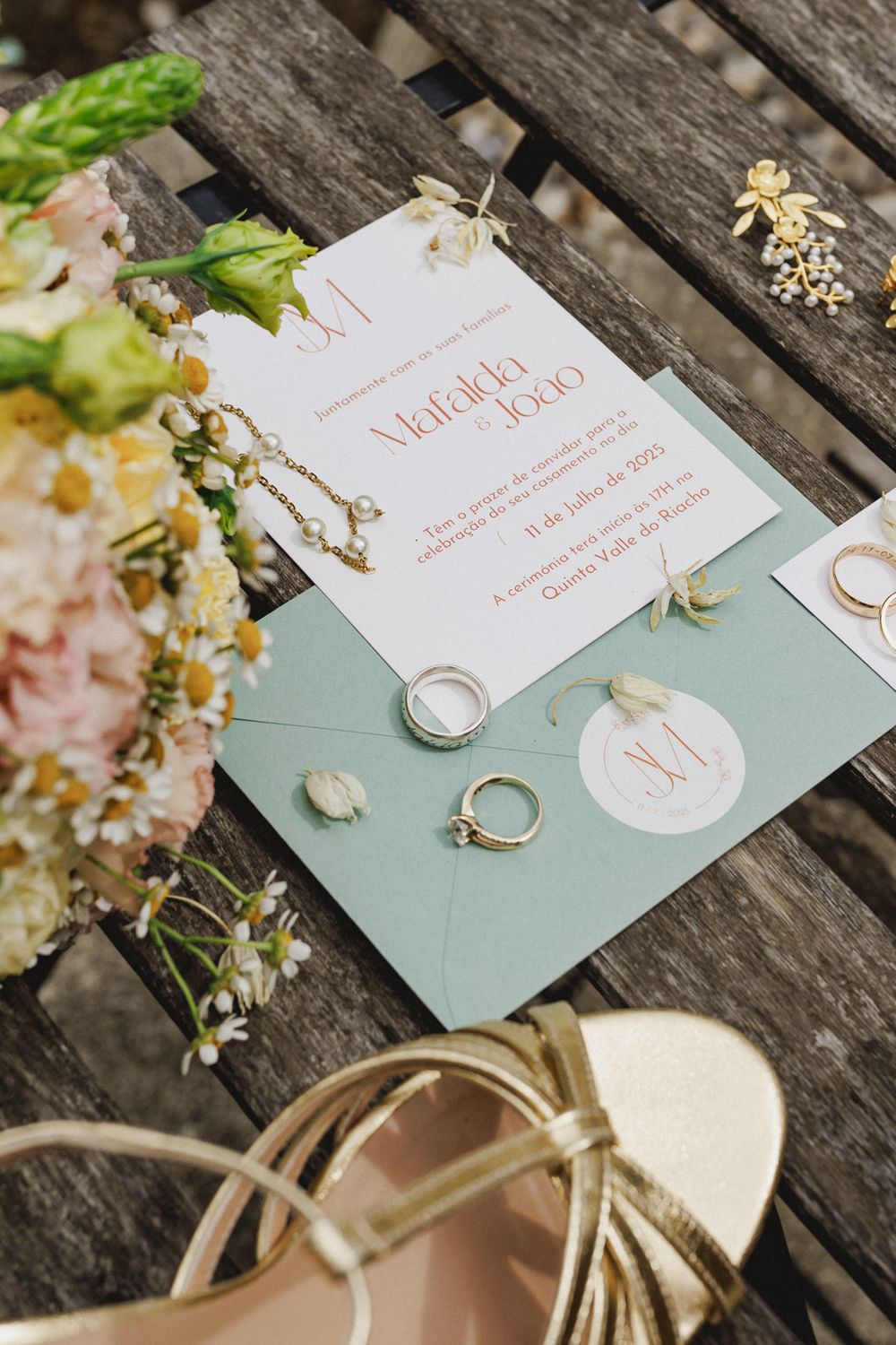 Wedding rings and invitation cards displayed on a mint green surface with delicate floral arrangements in a wedding in Lisbon