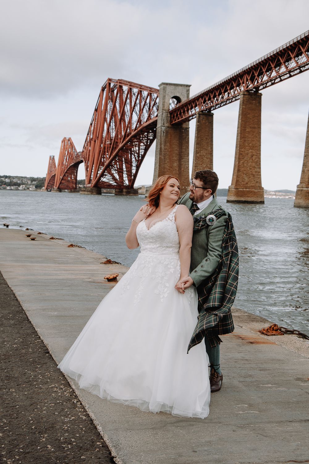 Newlywed couple posing by the historic Forth Bridge in Scotland.