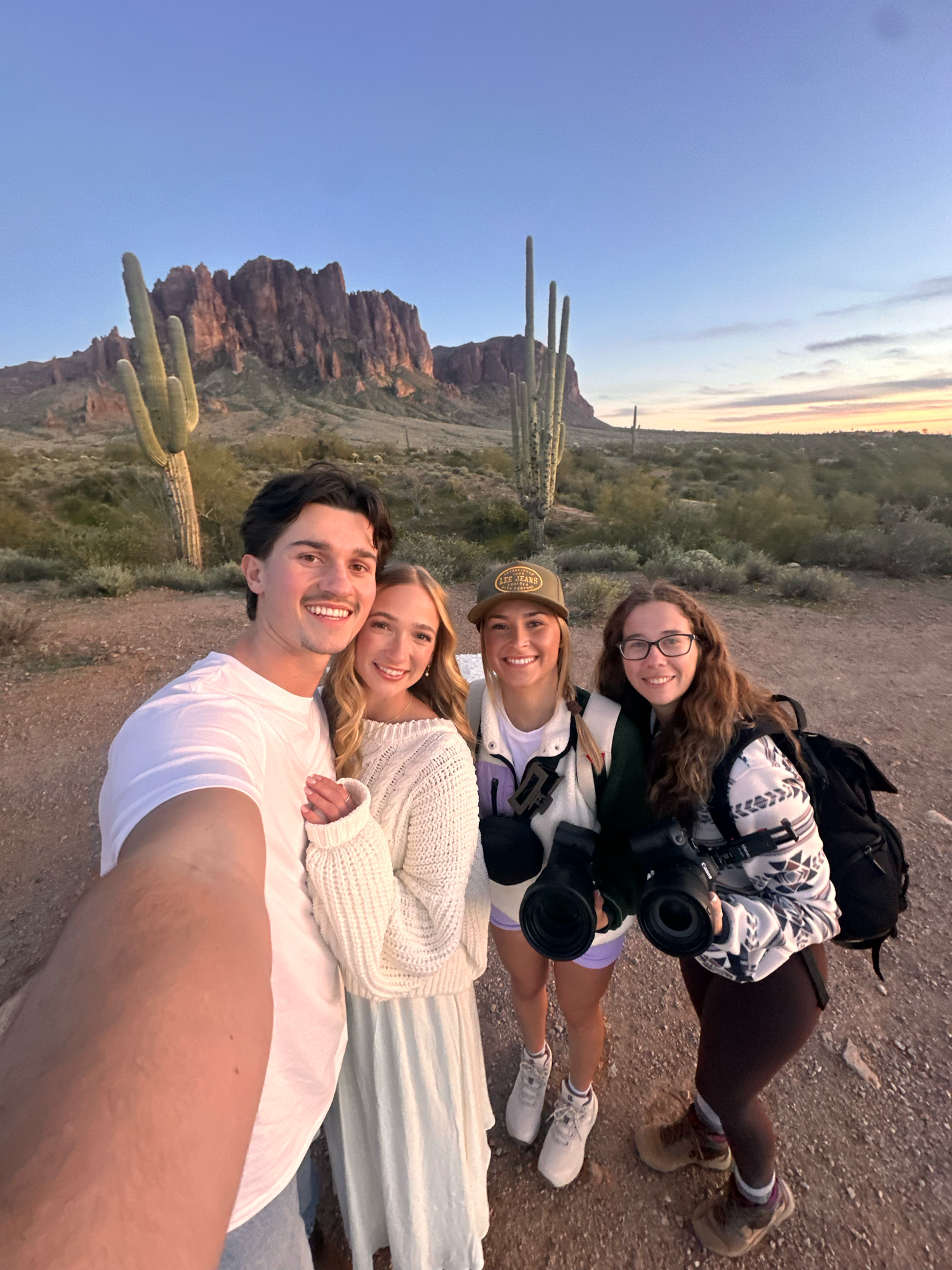 Group enjoying sunset in Arizona desert landscape with saguaro cacti and Superstition Mountains in background.