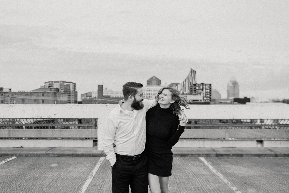 Two people dance together in an empty parking lot with an industrial cityscape visible in the background.