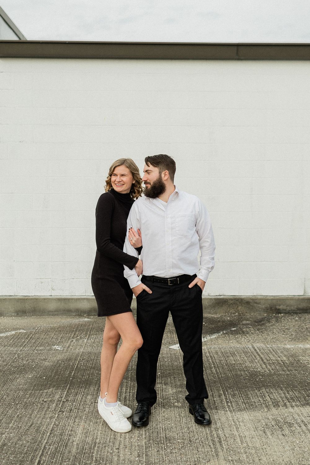 Couple in black and white outfits posing together against a concrete wall in an urban setting.