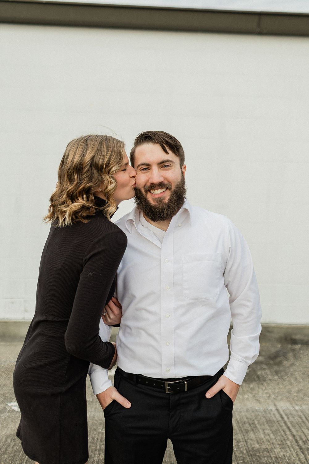 A couple shares intimate moments while posing against a white wall in contrasting black and white outfits.