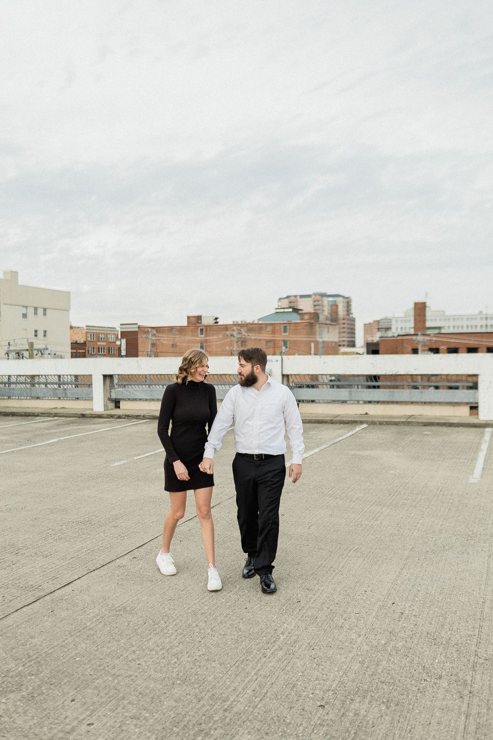 A couple strolls across a vast empty rooftop with city buildings on the horizon.