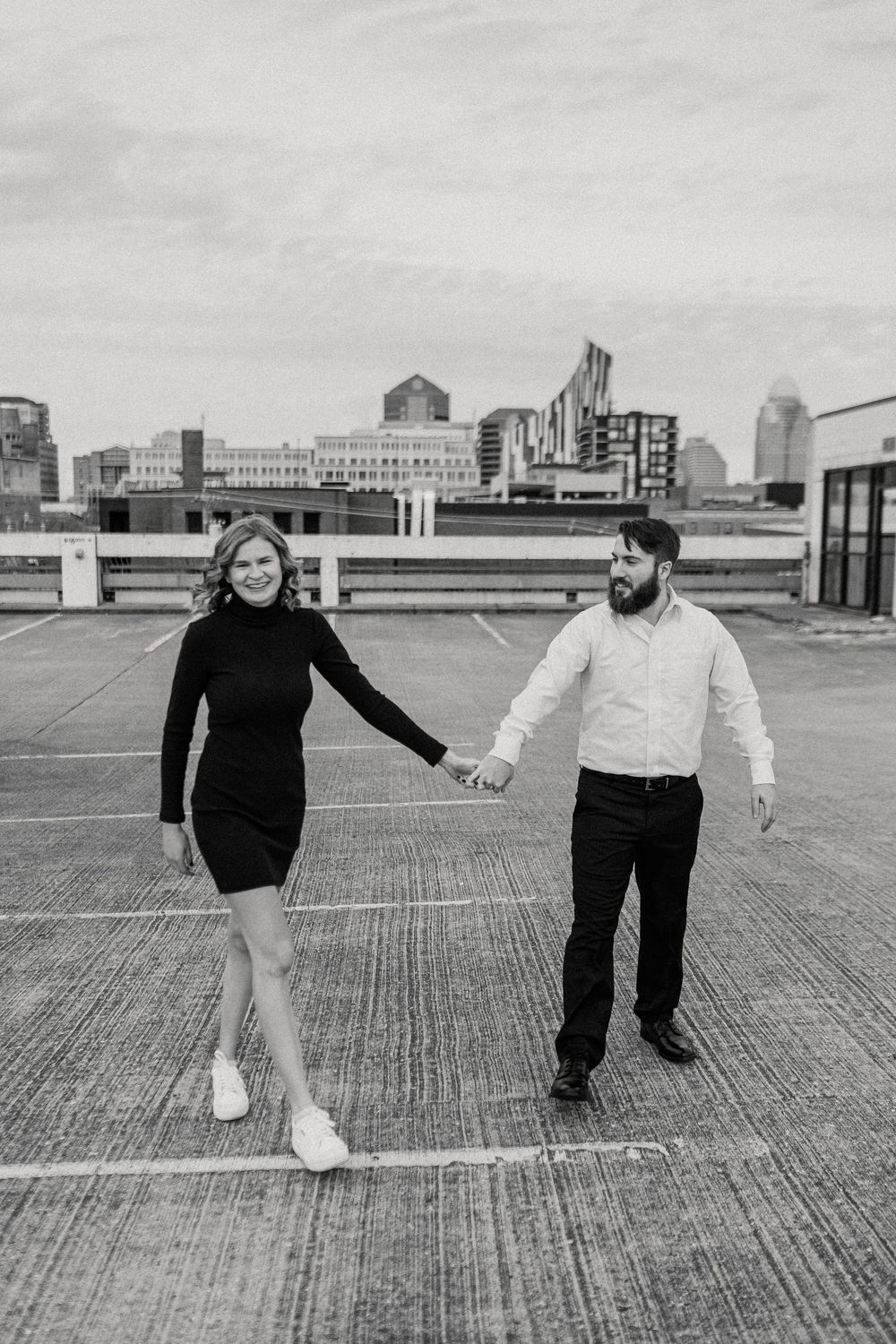 Two people in black and white outfits dance playfully on an urban rooftop with city buildings in the background.