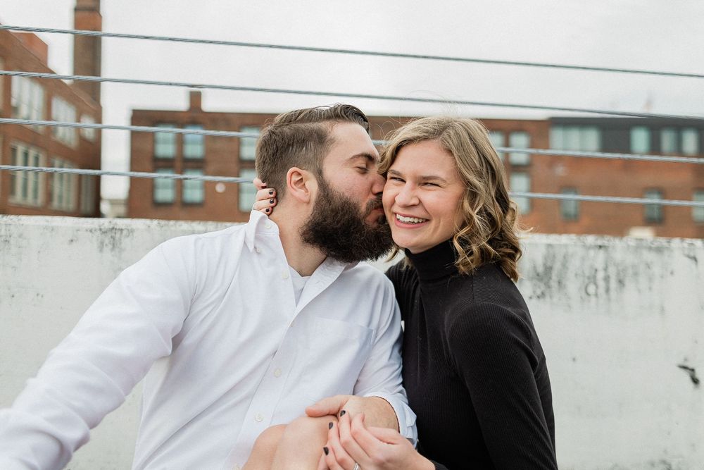 A couple shares playful moments during their engagement photoshoot with brick buildings in the background.