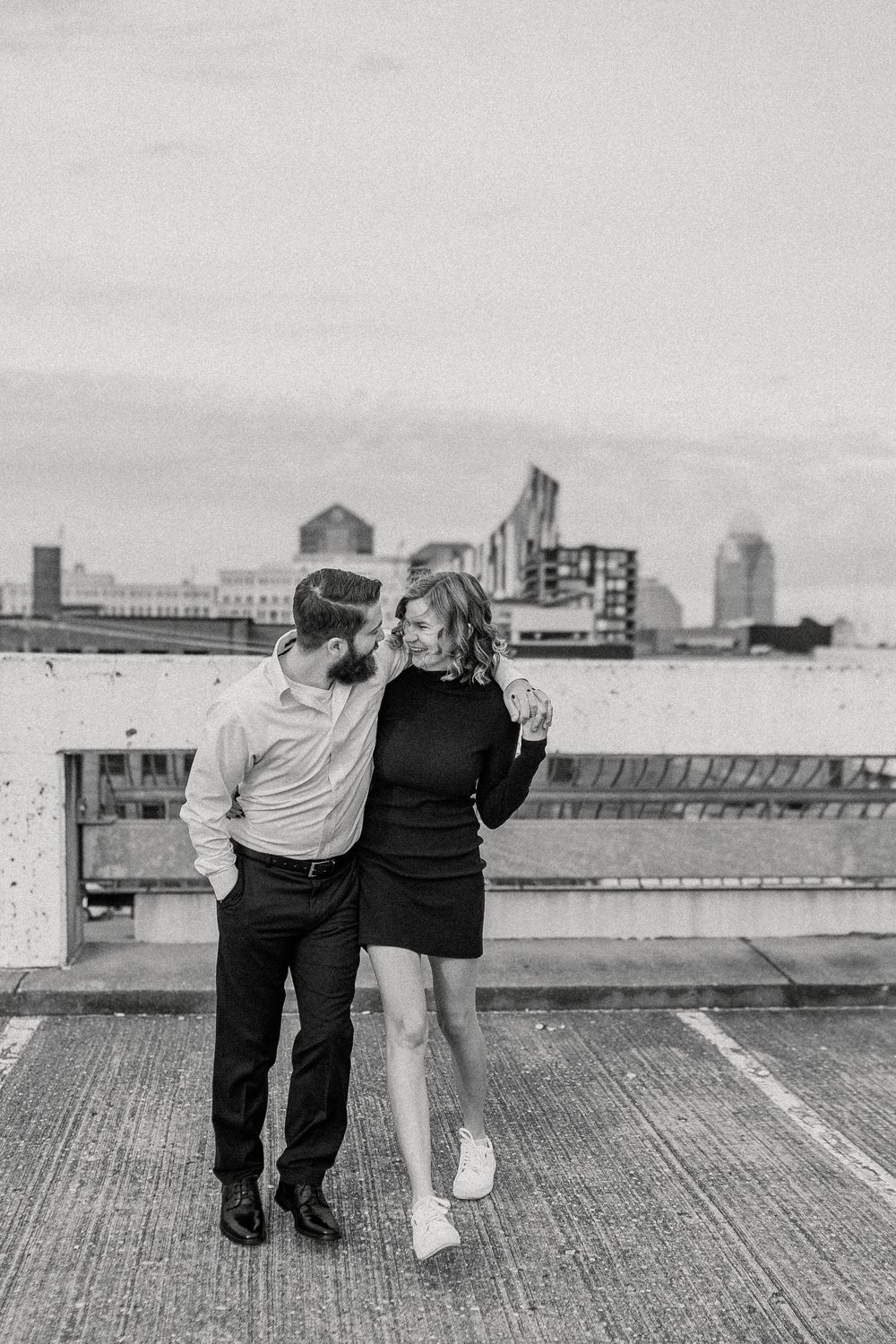 Black and white photo series showing a romantic couple sitting together on a rooftop with city buildings in background.