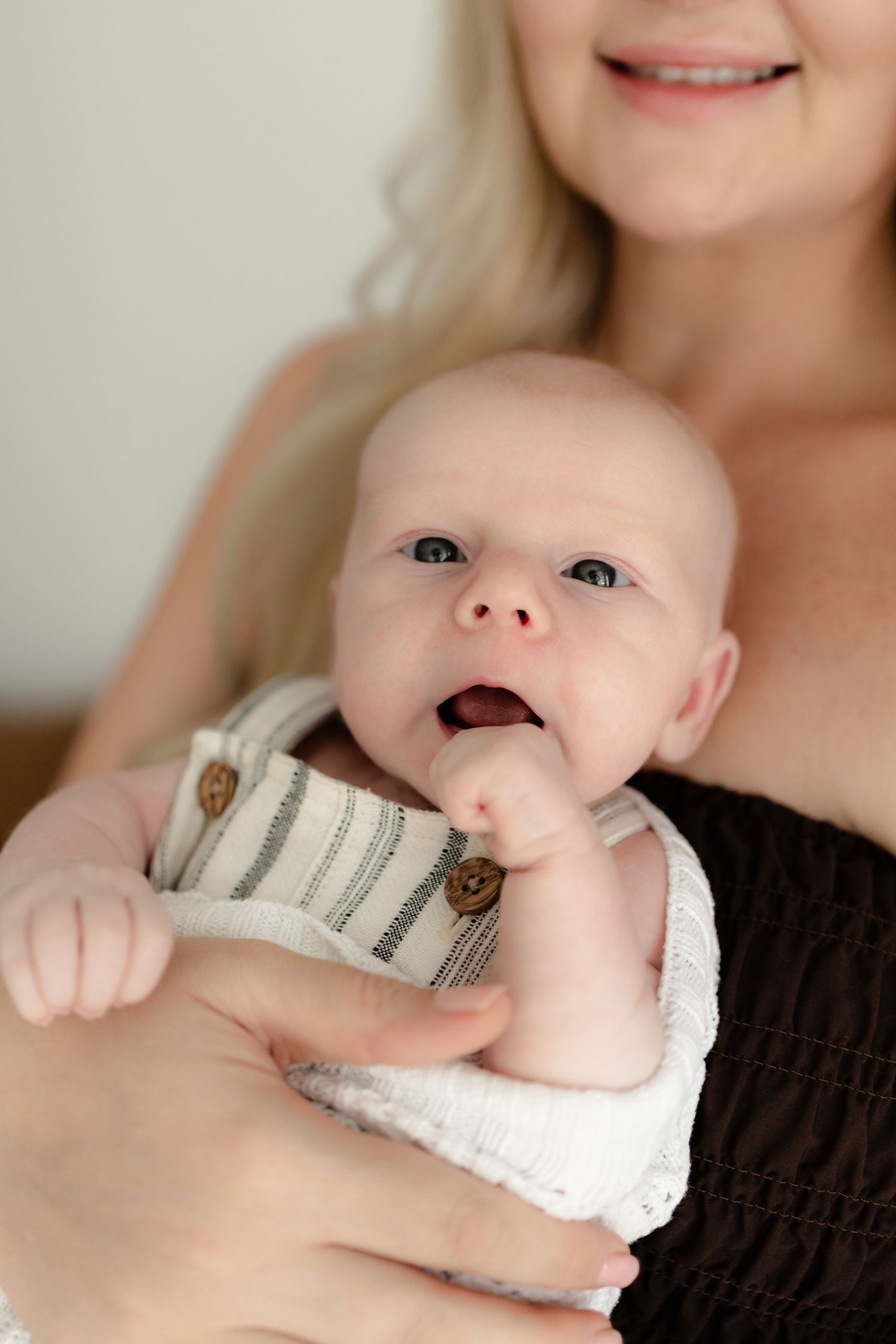 A small infant wearing a white sweater lies against a dark background while looking upward.