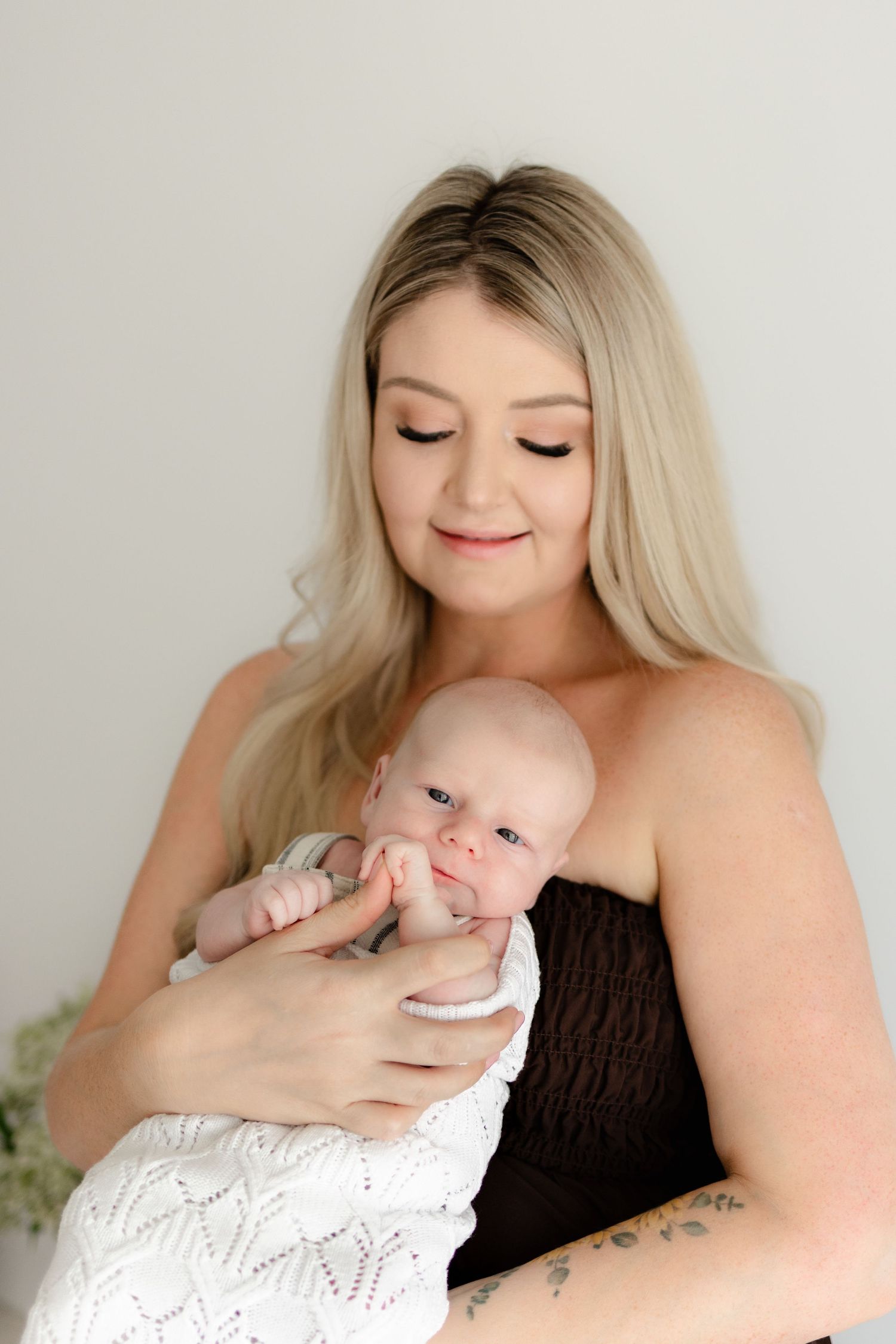 A tender moment between a parent and infant in white, with soft natural lighting creating an intimate portrait.