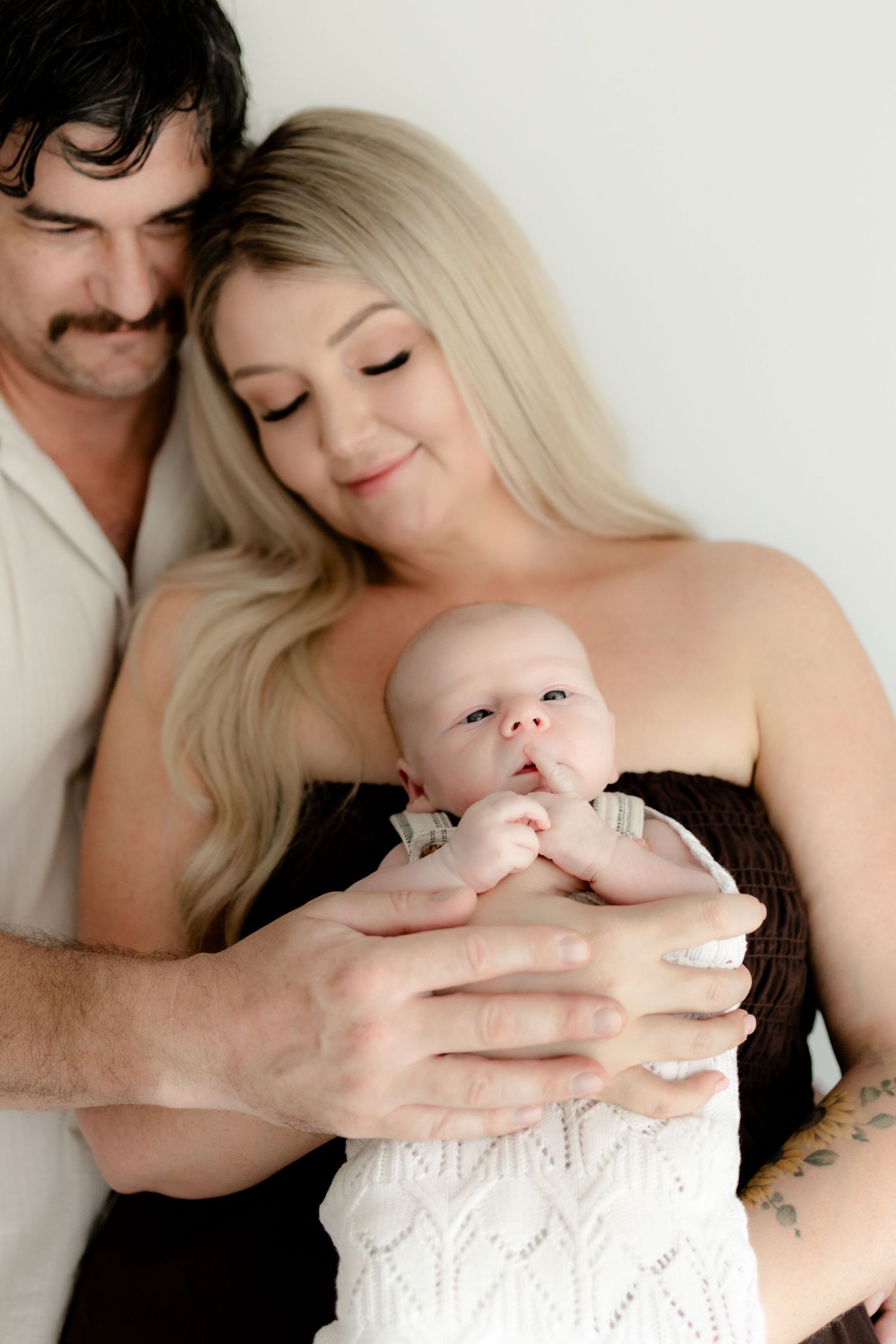 A couple holds their newborn baby together in an intimate portrait against a white background.