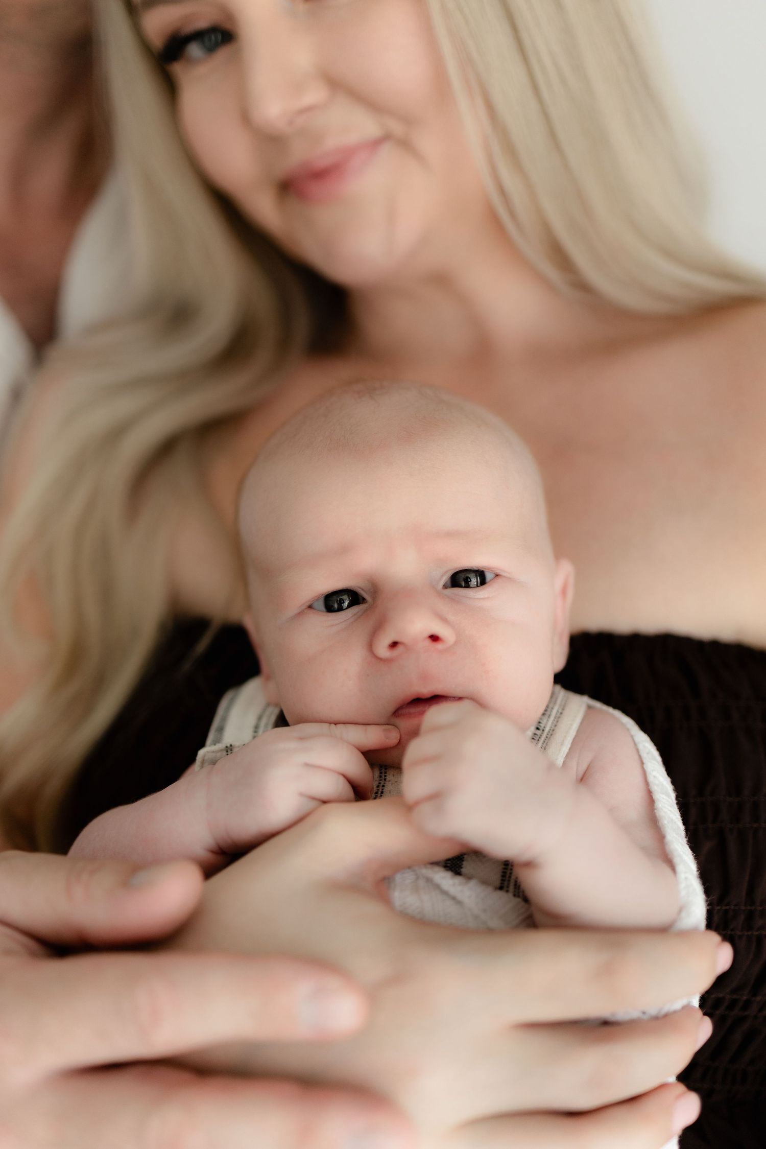 Close up portrait of a tiny baby being cradled in gentle hands against a light background.