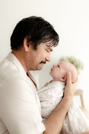 Gentle parental bonding moment with a newborn baby against a bright white background.