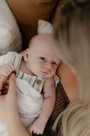 A newborn baby in white clothing rests peacefully against a soft brown background during a photography session.
