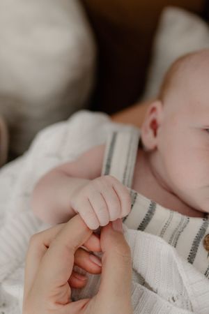 Close-up view of tiny infant hands grasping a white fabric against a soft background.