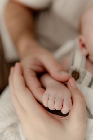 Close-up of tiny newborn baby fingers grasping gently against a soft white background.