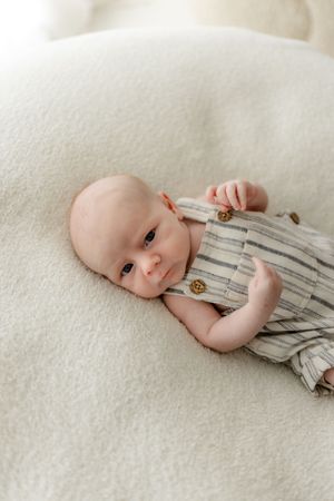 An infant rests on a white textured surface wearing a striped outfit.