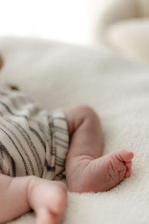 Delicate baby feet wrapped in striped fabric resting on white bedding.