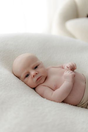 Close-up portraits of a newborn baby lying on soft white fabric.