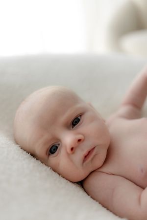 Close-up portrait of a baby lying on soft white bedding with bright natural light.