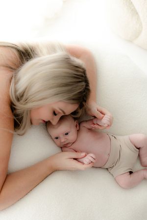 Mother and baby sharing a tender moment while lying together on white bedding.
