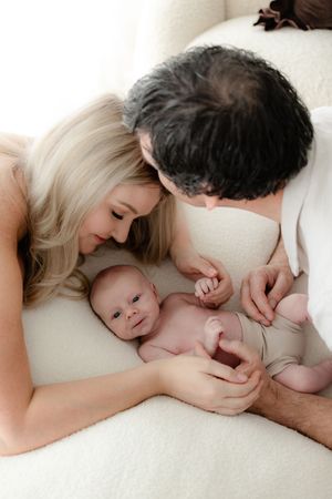 Intimate family portrait series showing parents cuddling with their baby on white bedding.