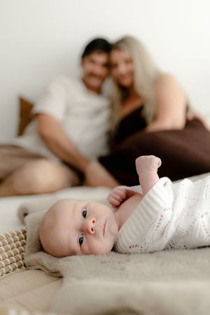Sweet family moment captured with newborn baby in foreground and parents resting in background.